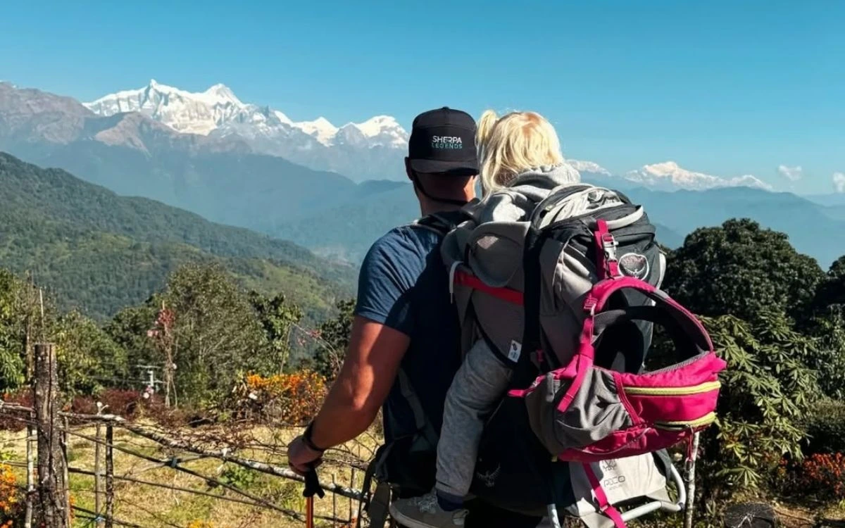 Trekker carrying a toddler in a backpack carrier overlooking the Himalayan range