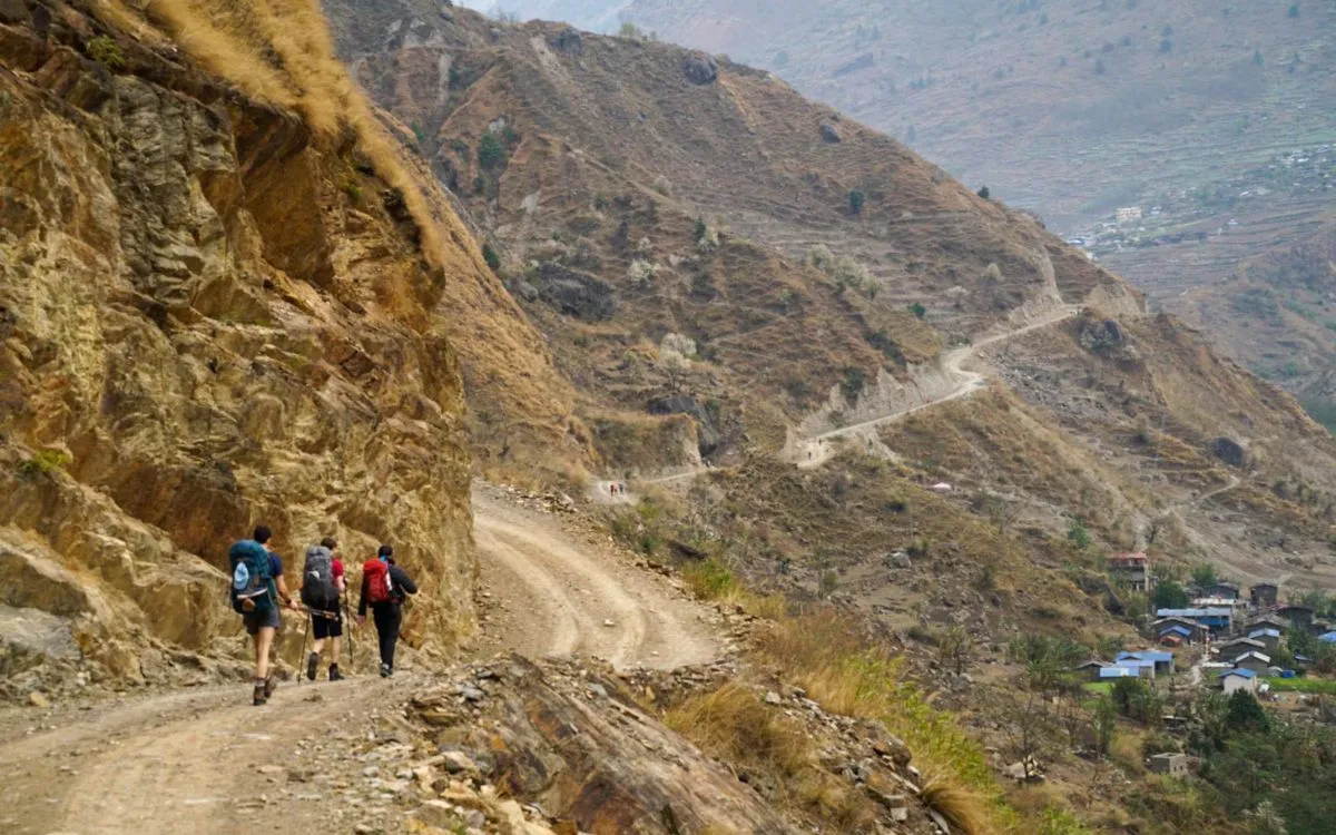 Trekkers hiking on mountain trail in Manaslu region Nepal with village in valley below