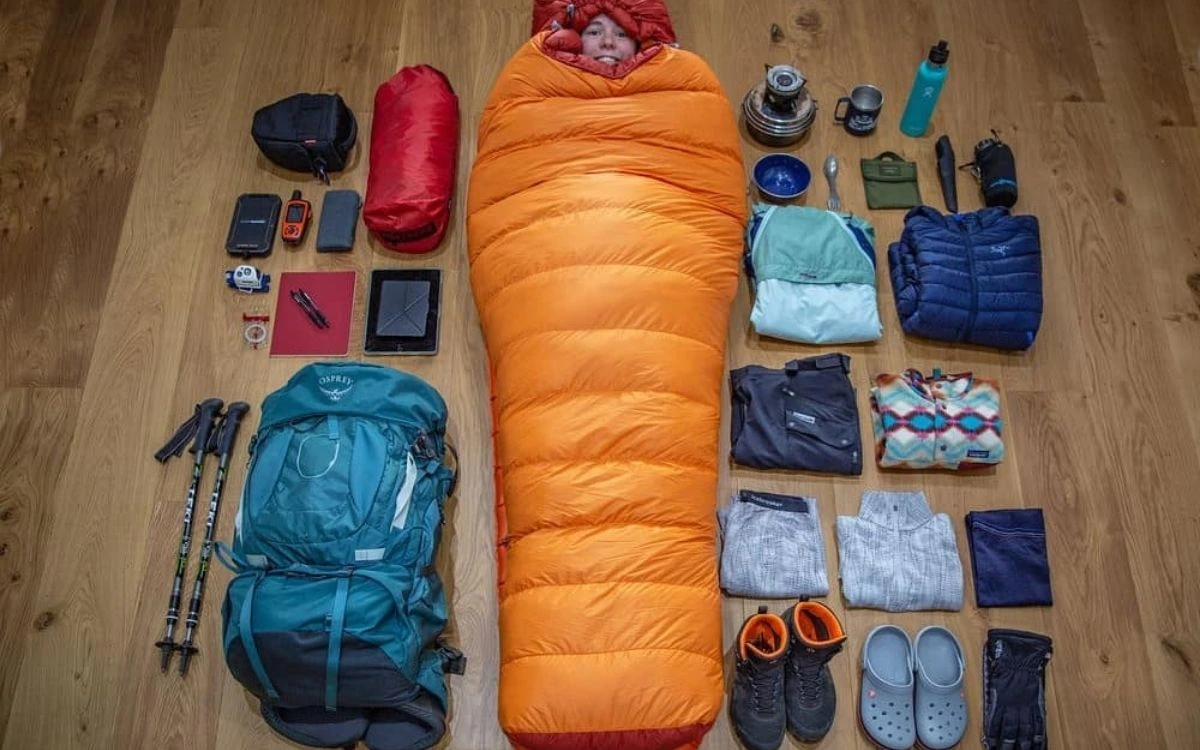 Complete trekking packing setup displayed on wooden floor with backpack, sleeping bag, hiking boots, clothing, and gear.