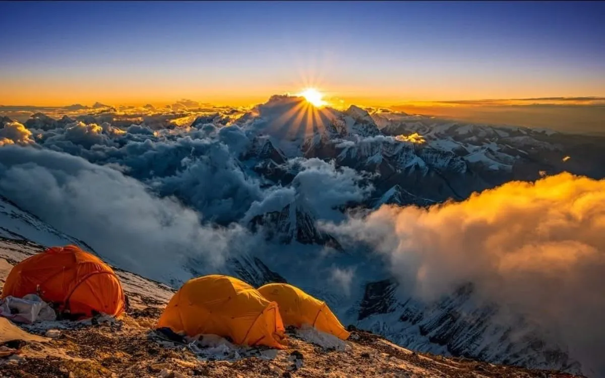 Sunrise from highest camp of Mt. Everest with orange tents and cloud-covered peaks