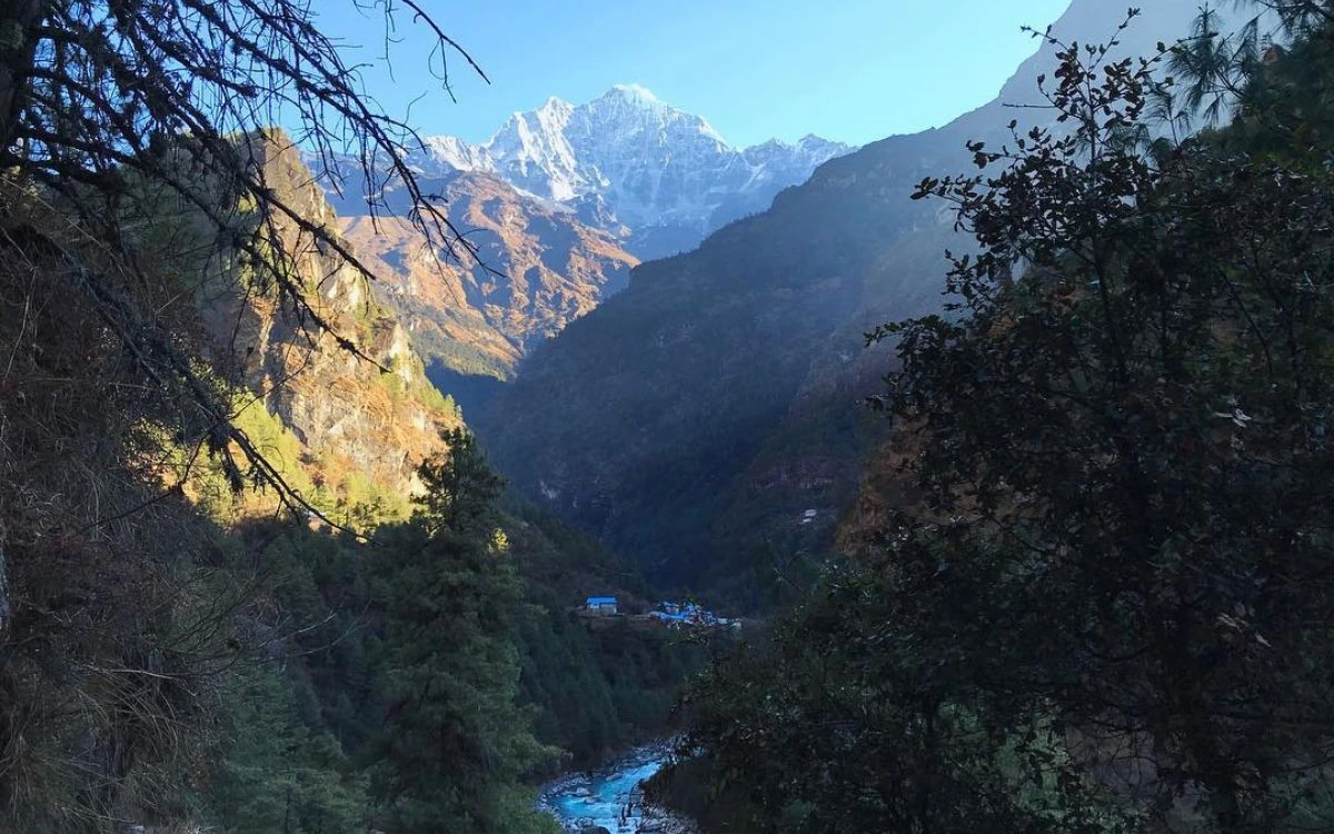 Small settlement nestled in deep valley with snow-capped Himalayan peak framed by trees