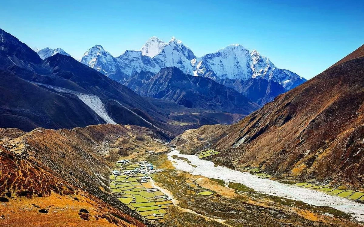 Aerial view of Pheriche village with green fields, a glacial river, and Everest region peaks behind