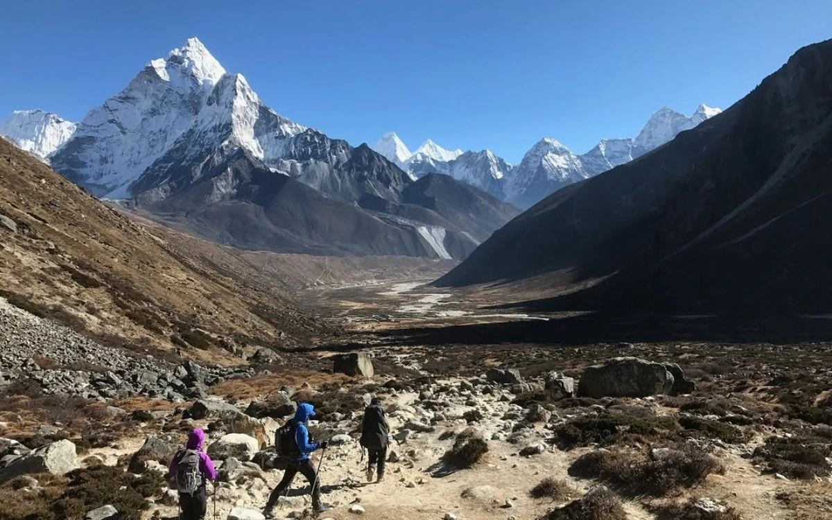 Three trekkers descending toward Pheriche valley with Ama Dablam towering above on the EBC trek