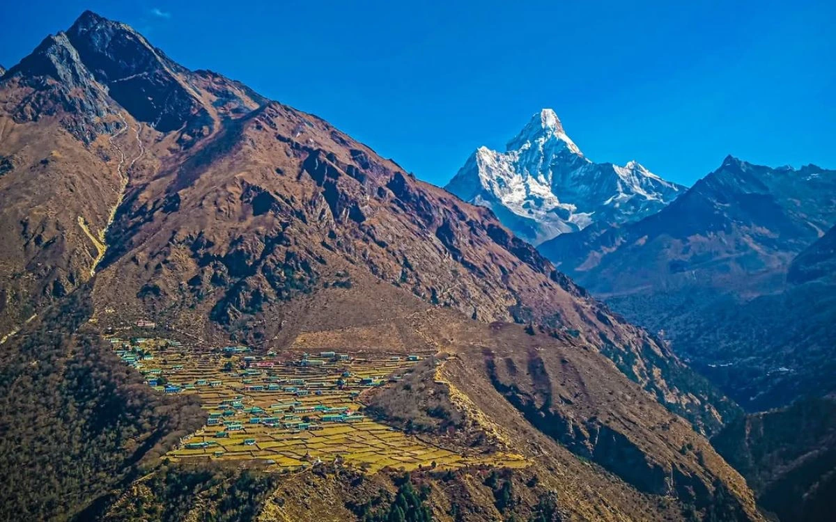 Aerial view of Phortse village with terraced fields on a mountain slope and Ama Dablam's iconic peak in the distance