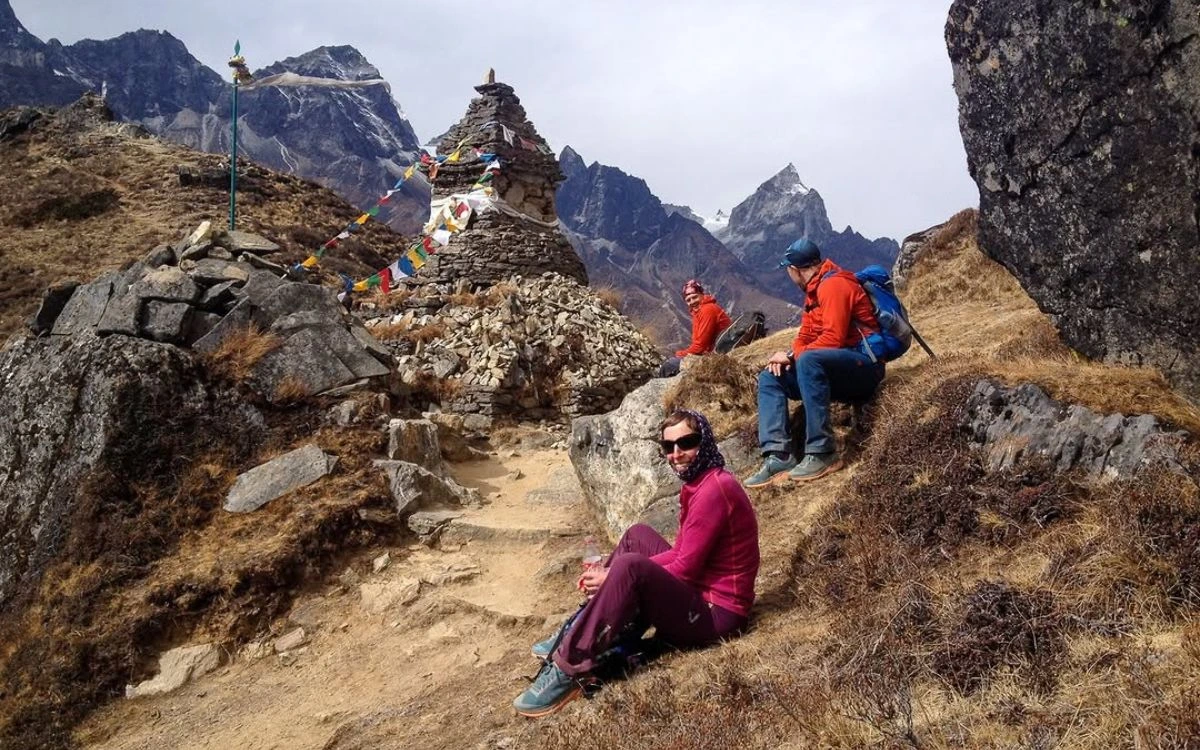 Trekkers resting beside a stone chorten draped in prayer flags on a high ridge above Phortse with jagged peaks behind