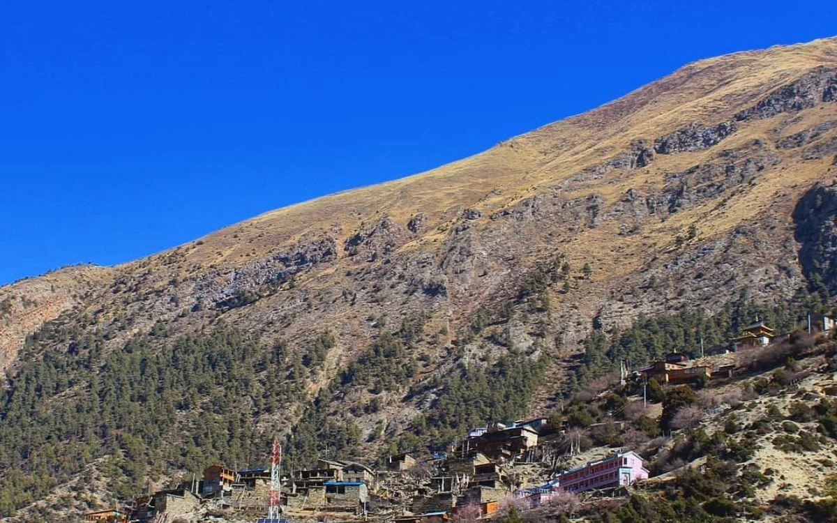 Traditional stone houses of Upper Pisang village perched on a steep hillside under a clear blue sky