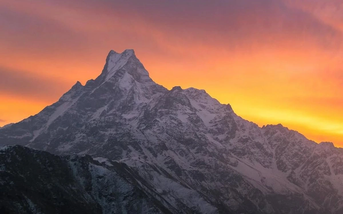 Fishtail (Machhapuchhre) mountain silhouetted against a vibrant orange and pink sunset sky