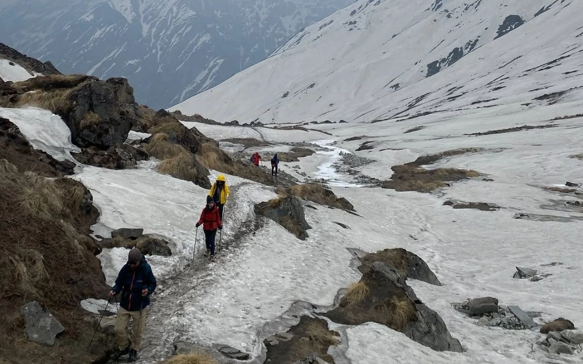 Trekkers carefully navigating icy snow-covered trail using trekking poles for stability