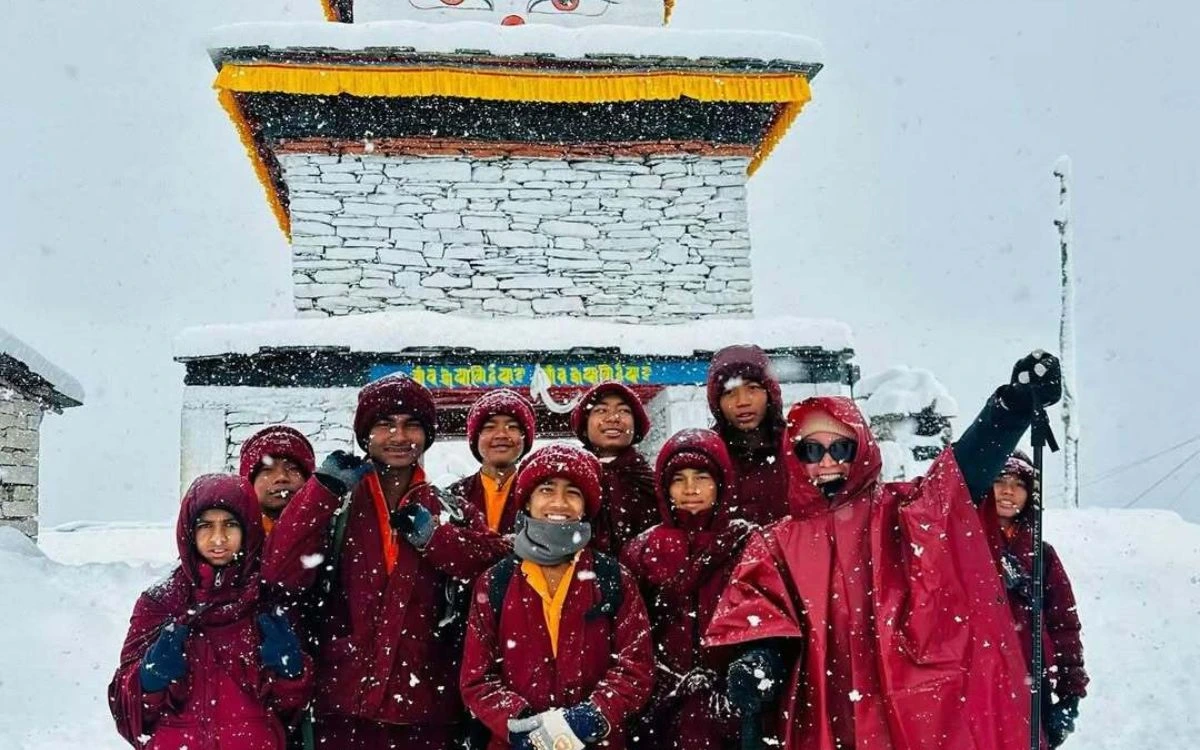 Monk and trekkers in red jackets posing together during snowfall at a village building in Samdo