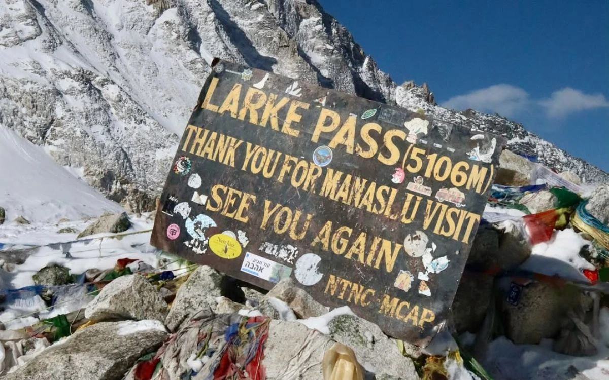 Larke Pass sign at 5,106 meters decorated with prayer flags and trekker stickers