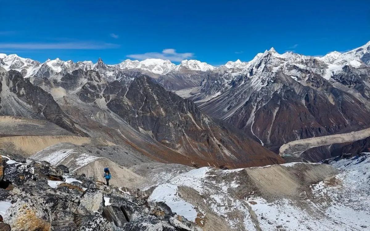 Trekker with blue backpack overlooking vast Himalayan glacier and mountain range