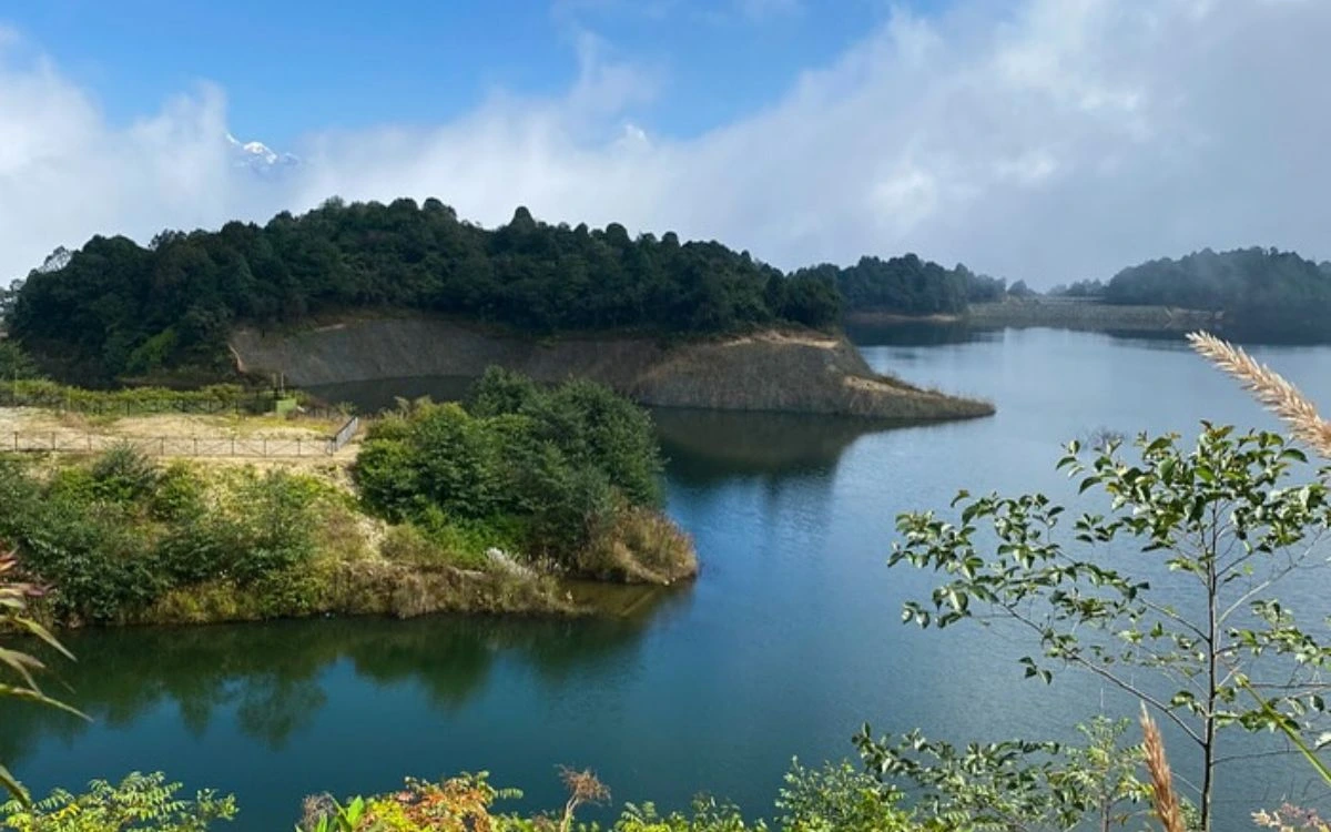 Tranquil blue reservoir with forested islands under partly cloudy sky within Shivapuri Nagarjun National Park, Kathmandu Valley