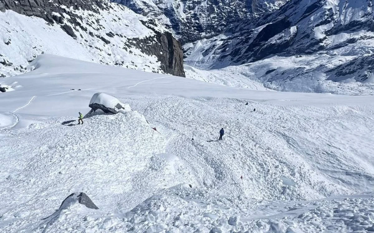 Climbers navigating avalanche debris on snow-covered Himalayan glacier trail