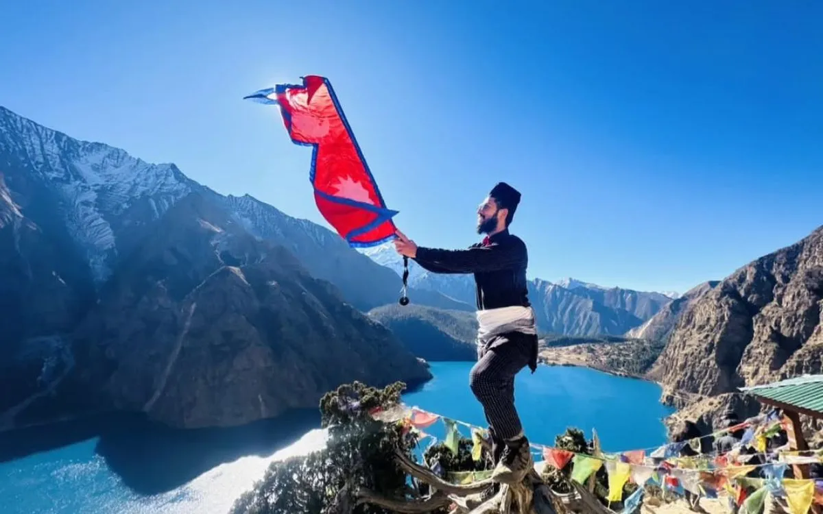 Person holding Nepal flag overlooking mountain lake and valleys