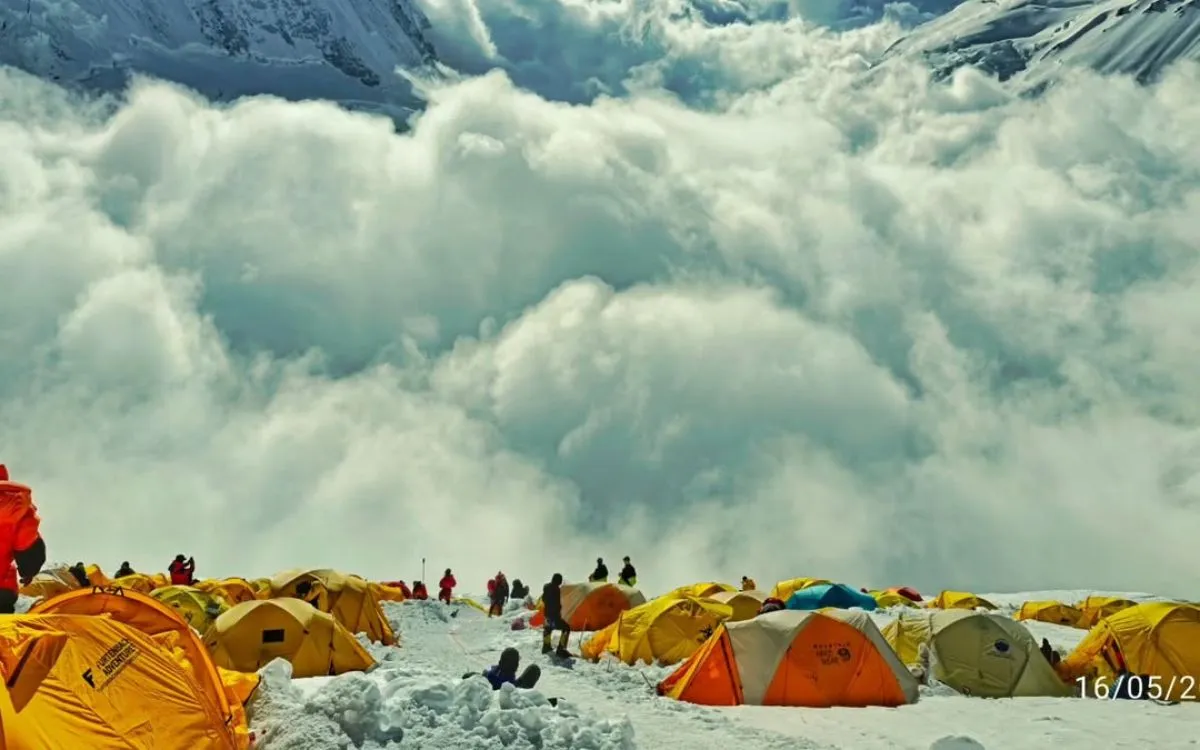 Colorful expedition tents at a high-altitude base camp with dramatic mountain peaks and clouds in the background