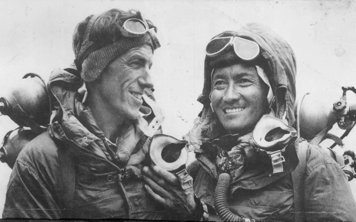 Historic black and white photo of two smiling mountaineers with climbing gear and oxygen equipment