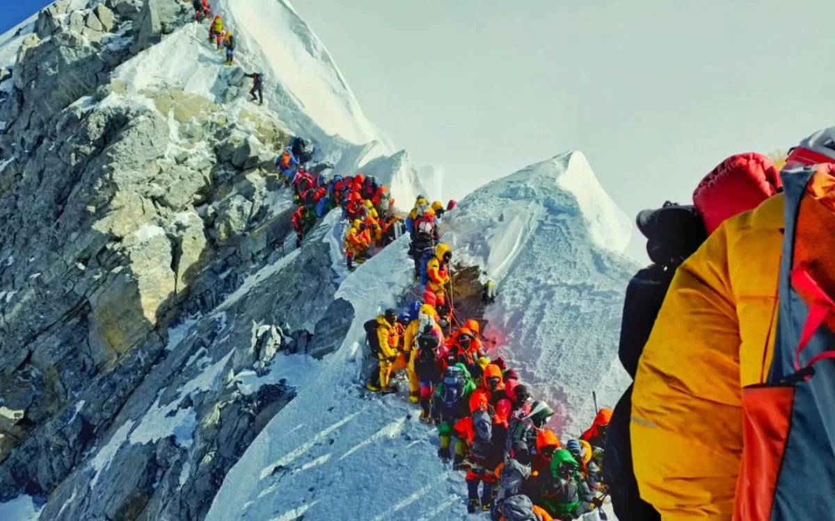 Long line of climbers in bright gear ascending a steep, rocky mountain ridge