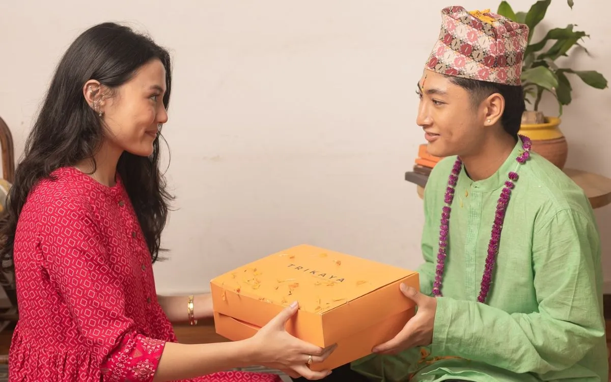 Woman in red kurta and young Siblings exchanging Tihar gift box with marigold garland during Bhai Tika ceremony