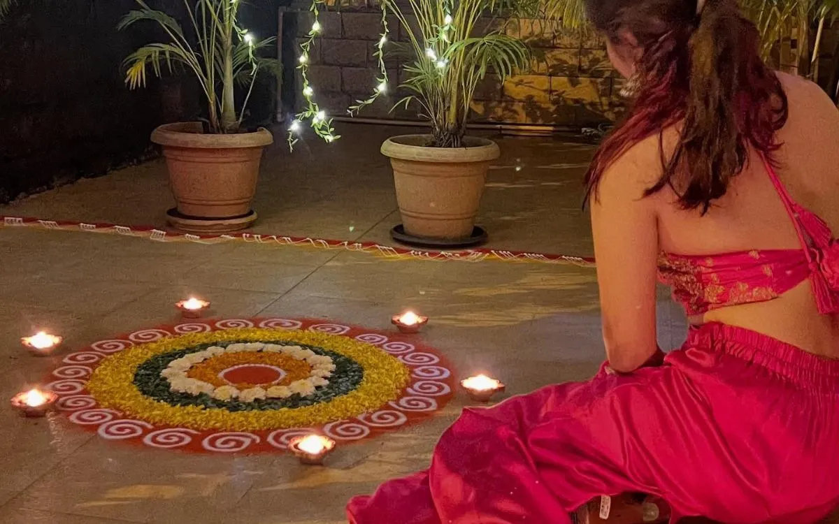 Woman in pink traditional dress sitting beside colorful rangoli with oil lamps celebrating Laxmi Puja during Tihar festival"