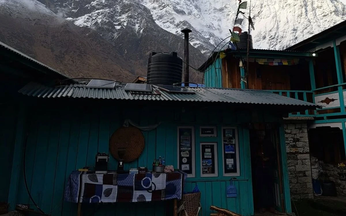 A teahouse with prayer flags nestled below snow-covered cliffs on a Nepal trek