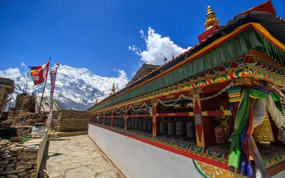 Colorful Buddhist monastery with prayer wheels and flags below a snow-capped Annapurna peak