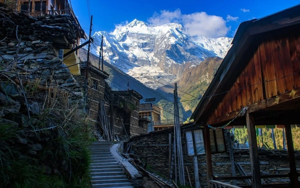Narrow stone-paved village lane with traditional houses and a snowy Annapurna peak at the end