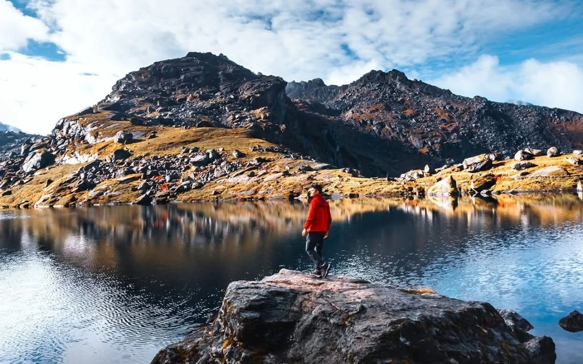 Hiker standing on rock beside mountain lake with reflected peaks