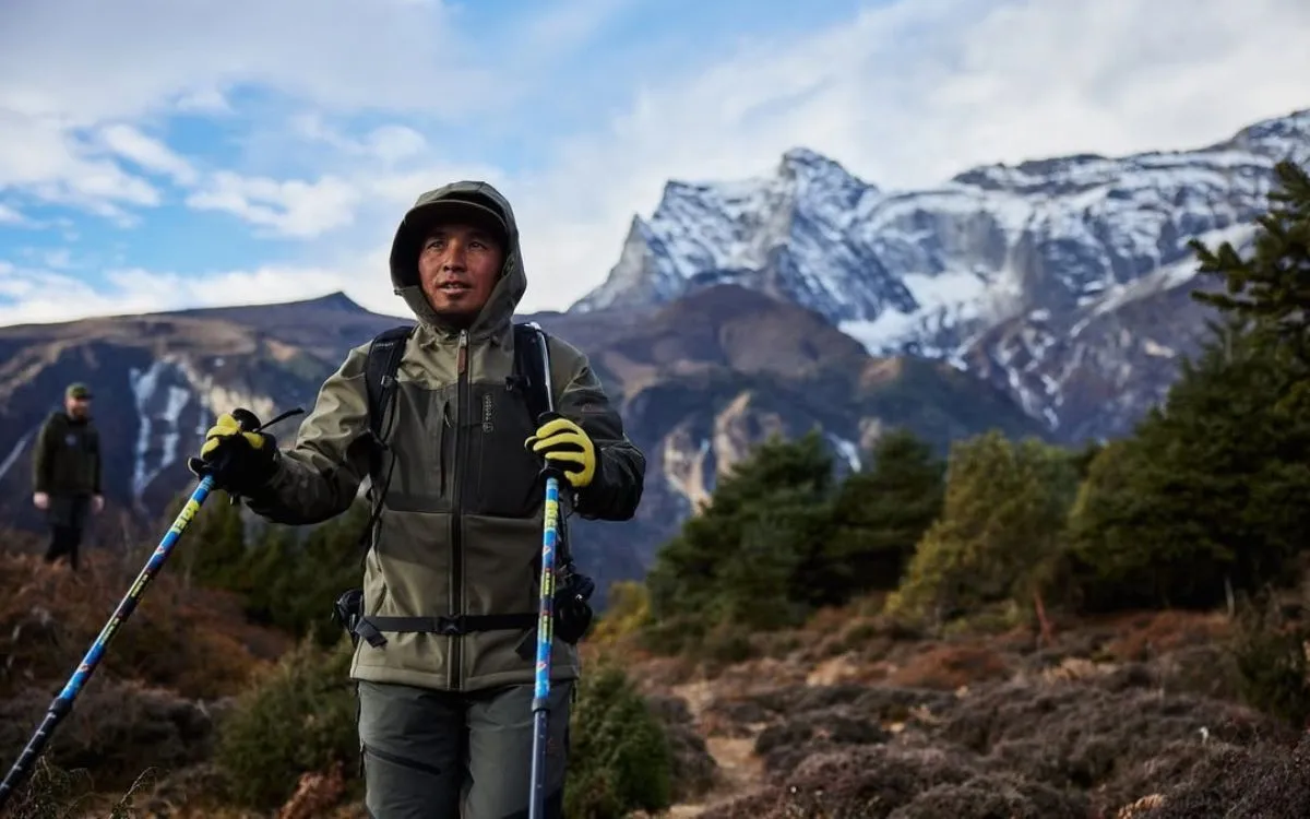 Trekker with blue trekking poles posing in front of snow-capped mountains