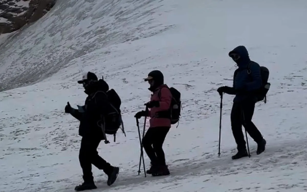 Three hikers silhouetted against snowy slope using trekking poles