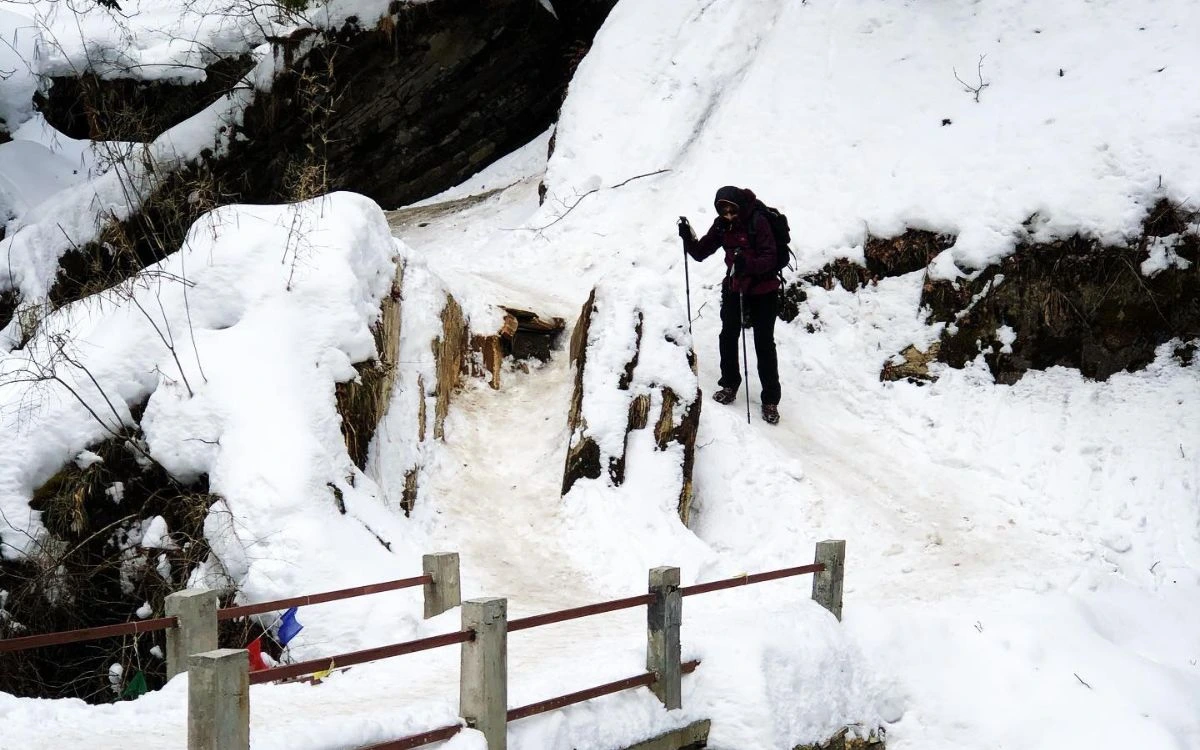 Trekker crossing a snowy footbridge on a December trek in Nepal