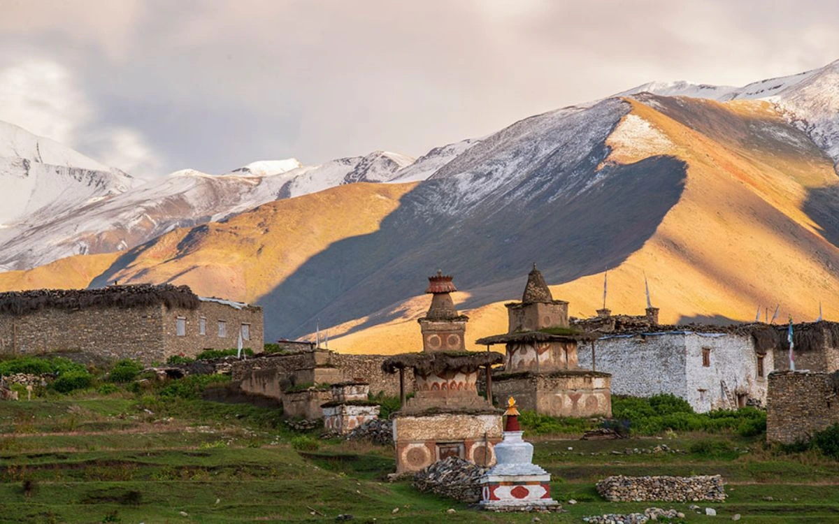 Ancient stupas and stone buildings at golden hour with snow-streaked mountains in Upper Dolpo