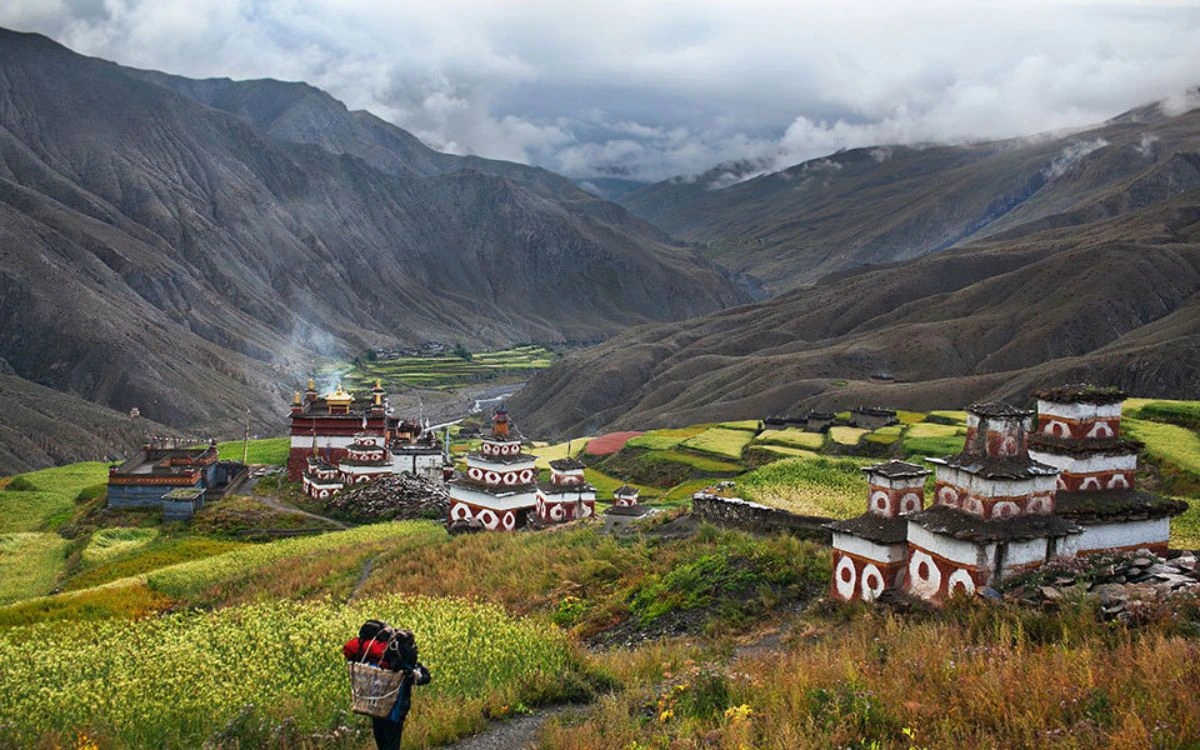 Porter approaching a Bon monastery complex with red and white chortens in a remote Dolpo valley