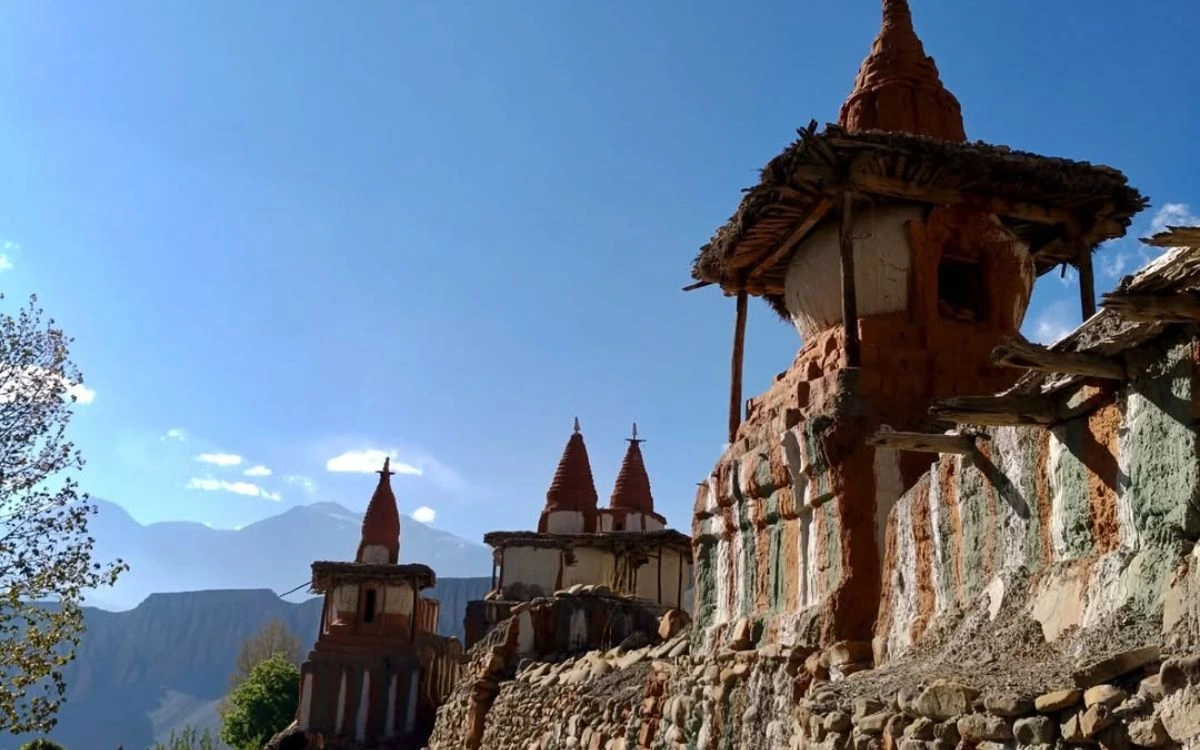 Weathered red-clay stupas with thatched roofs against a clear blue sky in Upper Mustang