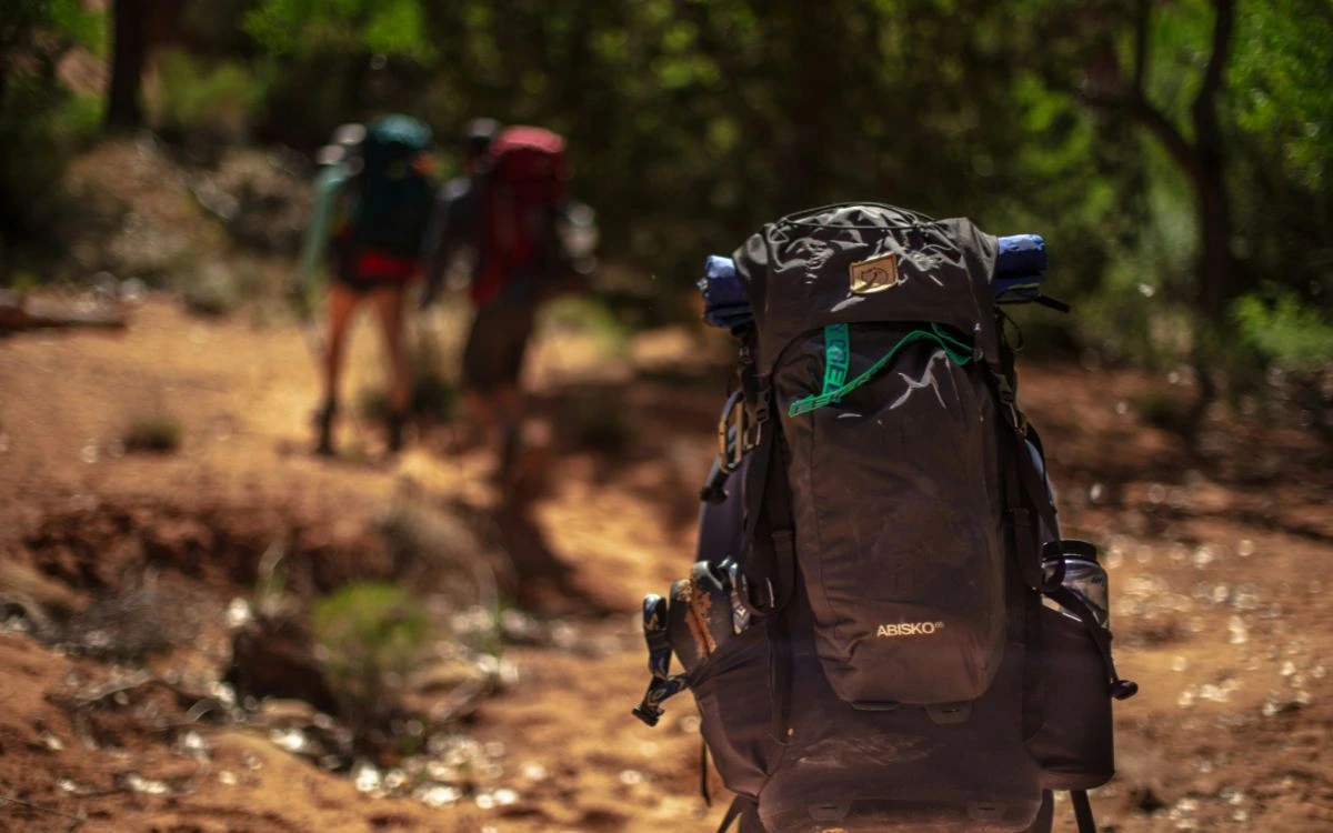 Trekking backpack on trail with hikers walking ahead through forest
