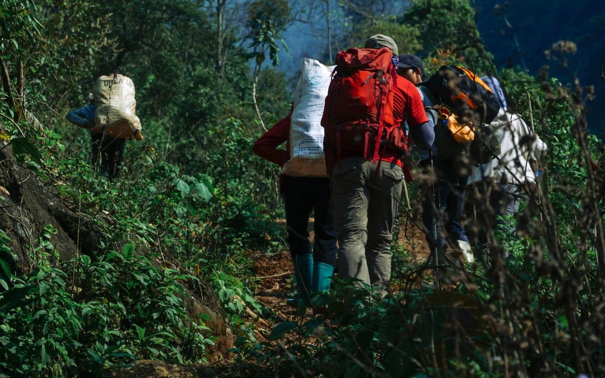 Porters and trekkers hiking on forest trail in Nepal with heavy backpacks