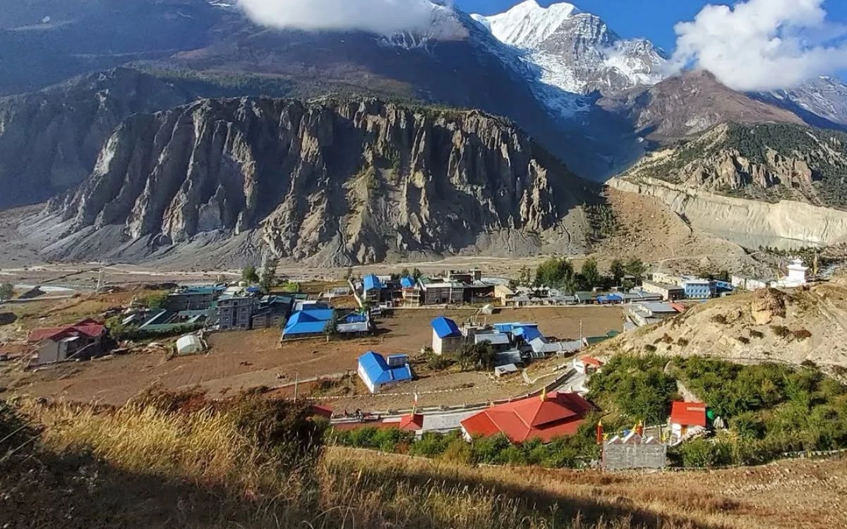 Aerial view of Yak Kharka village with colorful rooftops set against dramatic Himalayan cliffs and snow-capped peaks