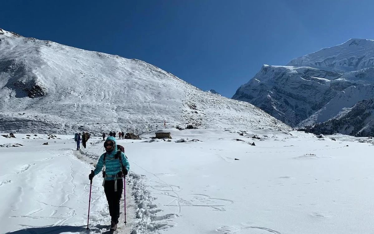 A trekker with poles walking through deep snow toward Thorong La Pass on the Annapurna Circuit
