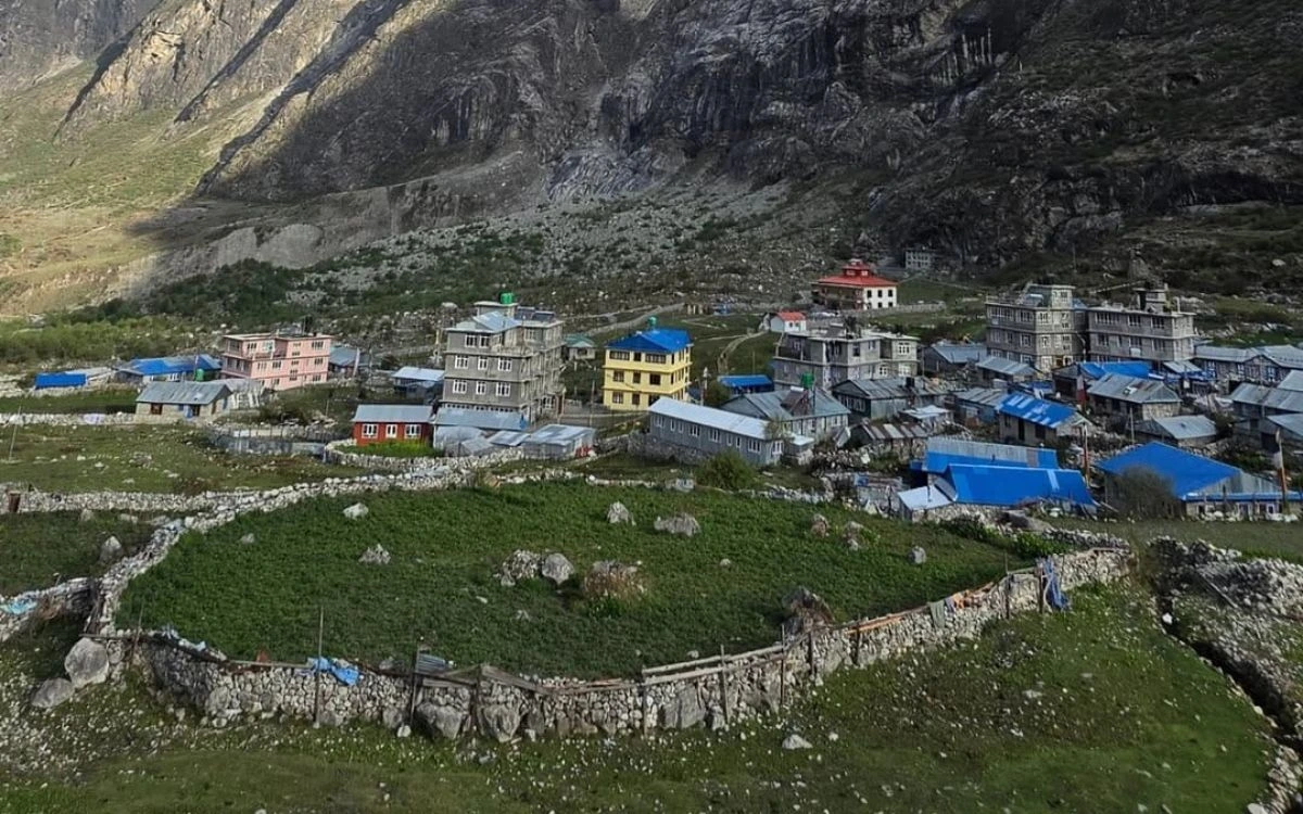 A small Himalayan teahouse village nestled at the foot of massive, rugged stone cliffs.