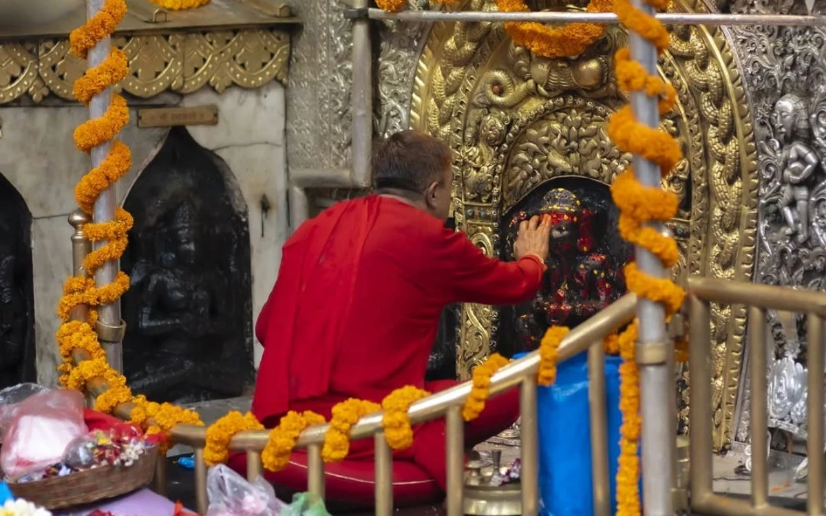A priest in red robes performing a ritual at the sacred Goddess Kali shrine.