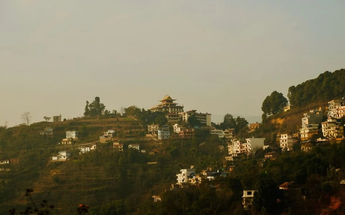A scenic view of traditional houses and a monastery nestled on the forested hills of Pharping.