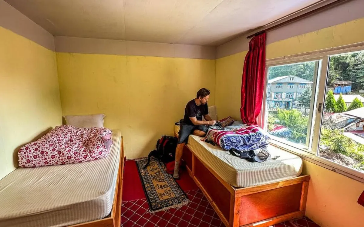 Simple guesthouse room with two beds, yellow walls, and mountain view through window