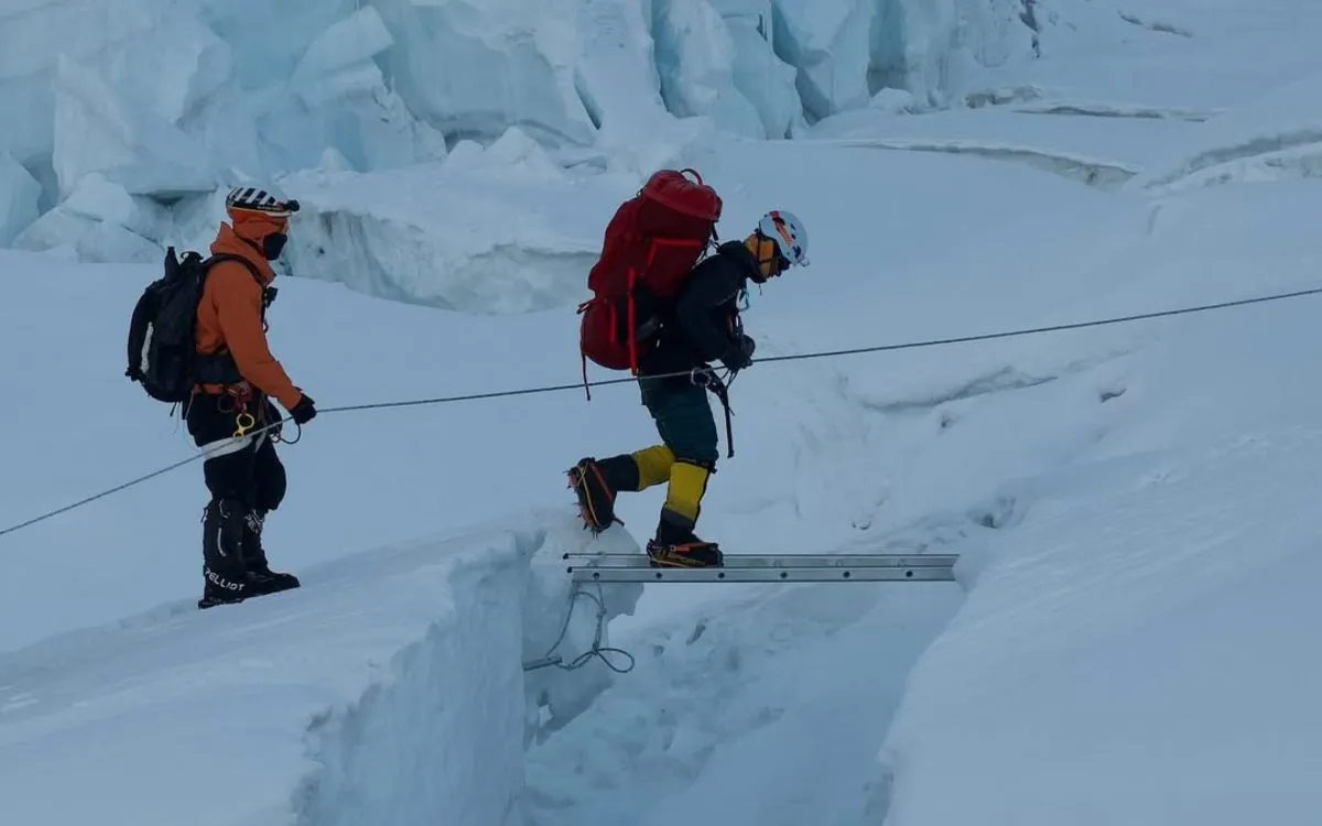 Mountaineers crossing aluminum ladder over deep crevasse in Khumbu Icefall on Mount Everest