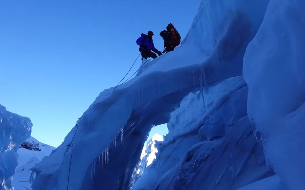 Two climbers climbing down blue ice wall in Everest icefall with safety ropes