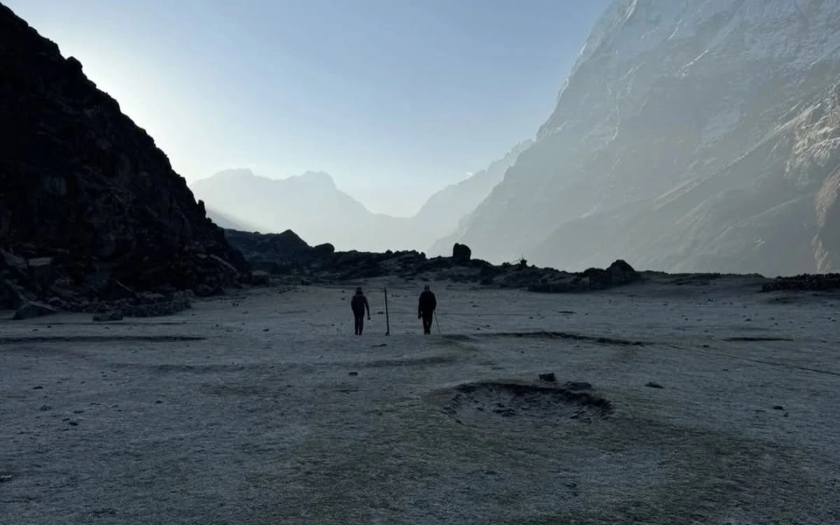 Two trekkers walking through a vast, isolated plain valley flanked by high mountain ridges.