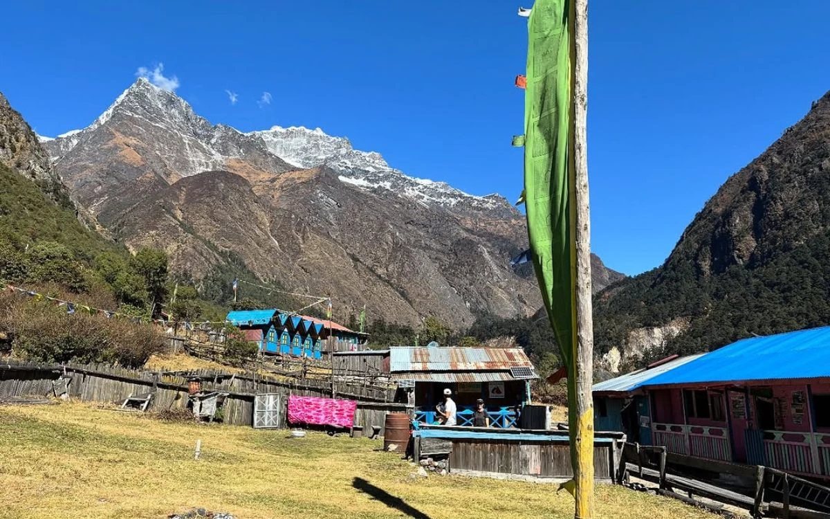 A remote teahouse village with prayer flags on the Kanchenjunga Trek with a snow-capped peak above