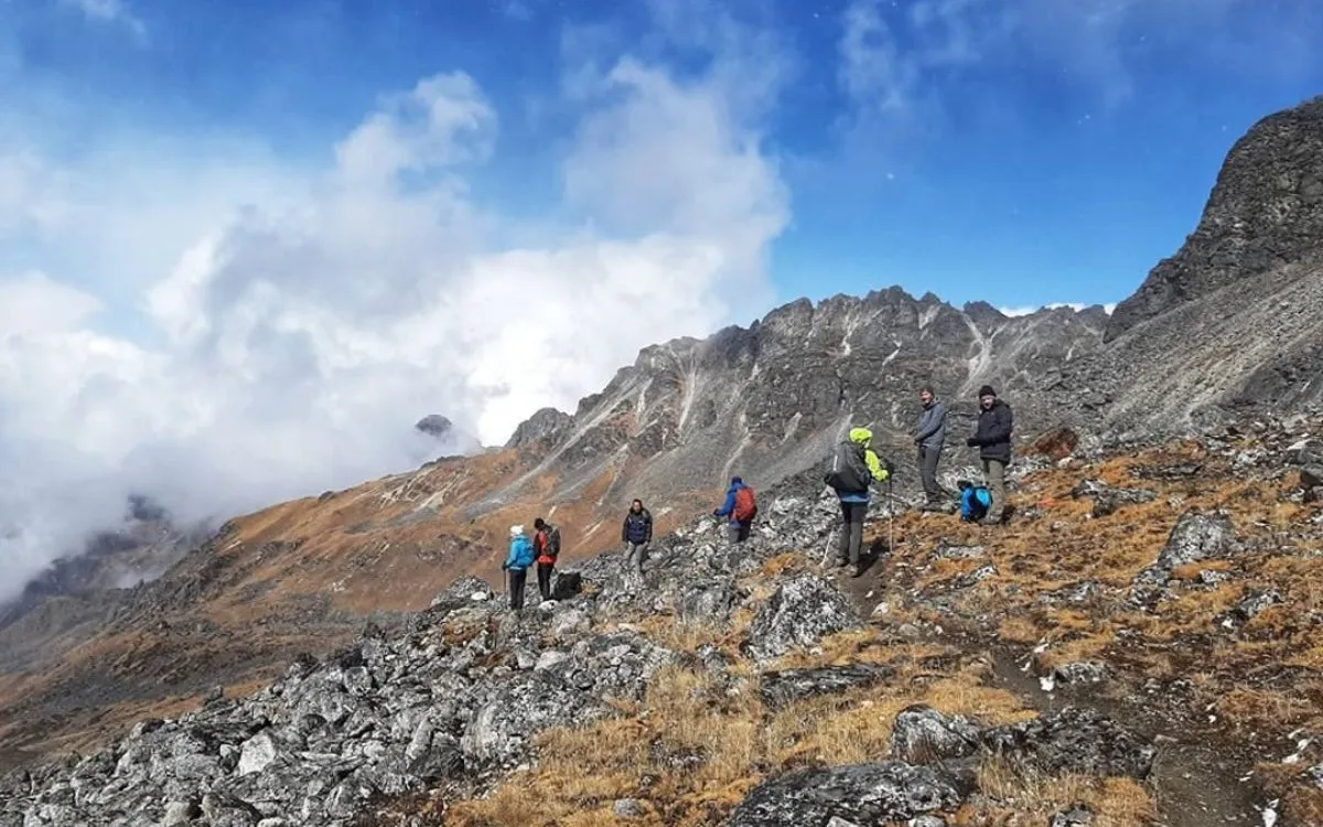 A group of trekkers resting on a rocky high-altitude ridge with clouds rolling in on the Kanchenjunga Trek