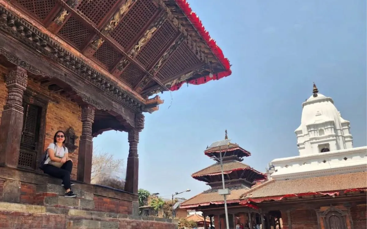 Woman by a wooden building, temples in background around Kathmandu Durbar