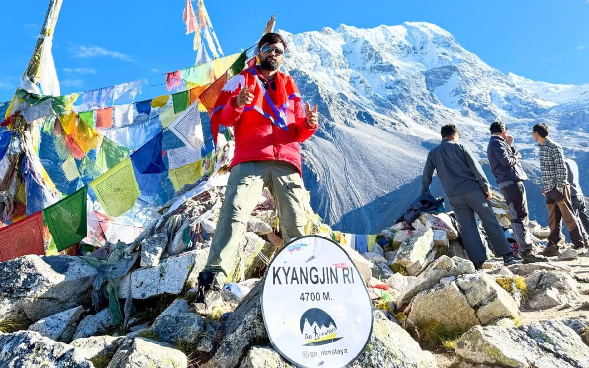 Hiker at Kyanjin Ri summit sign at 4700m with prayer flags and mountain backdrop