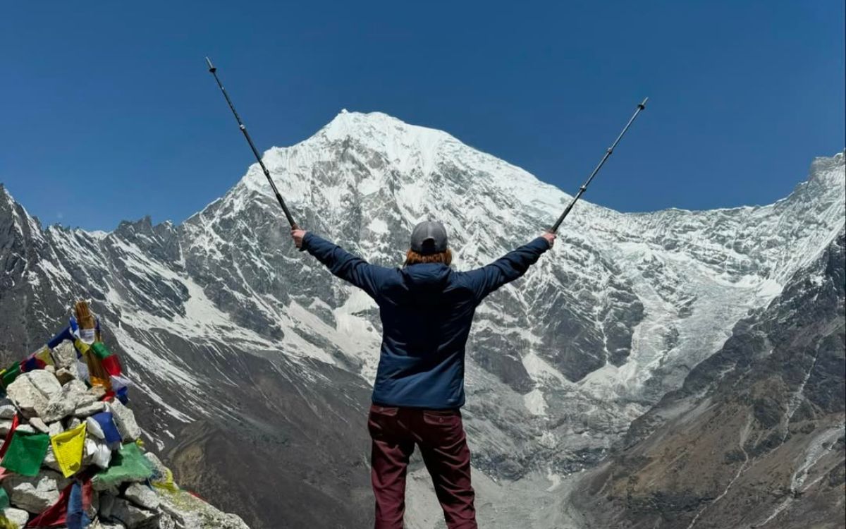 Trekker celebrating at Kyanjin Ri viewpoint with arms raised facing Langtang Lirung peak