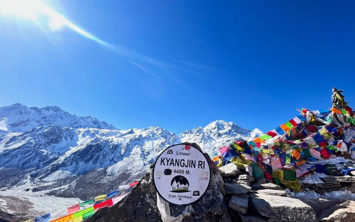 Kyangjin Ri viewpoint sign at 4400m with colorful prayer flags and Himalayan peaks